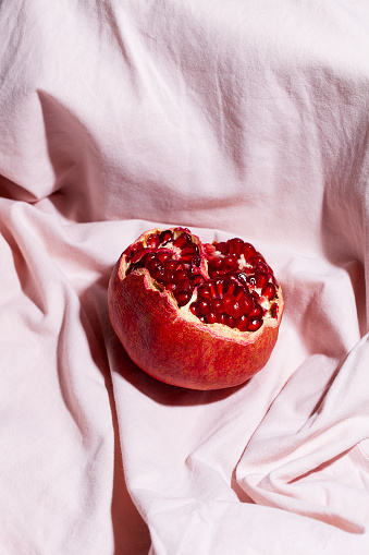 One red pomegranate on pink textile background. Modern fruit still life