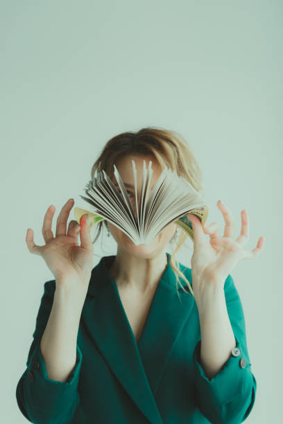 Young blond woman covering her face with a book.