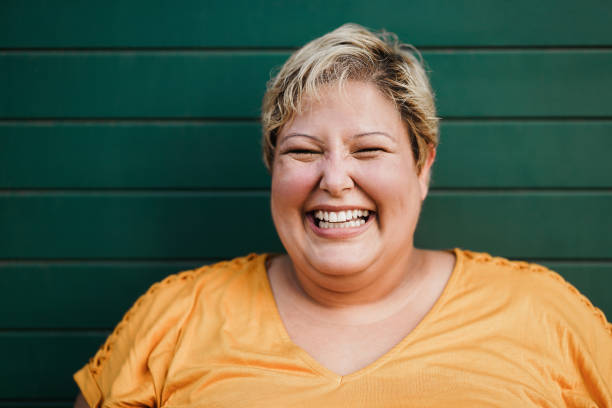 ritratto di donna curvy sorridente sulla macchina fotografica all'aperto con sfondo verde - focus sul viso - common foto e immagini stock