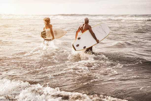 istock Father and son running on the beach at sunset for surf training - Focus on right man 1304711610