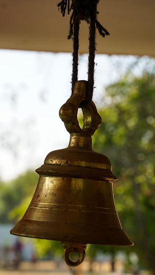Bronze bell in indian temple in the green crops blur background. Hindu temple brass bell hanging in gold color