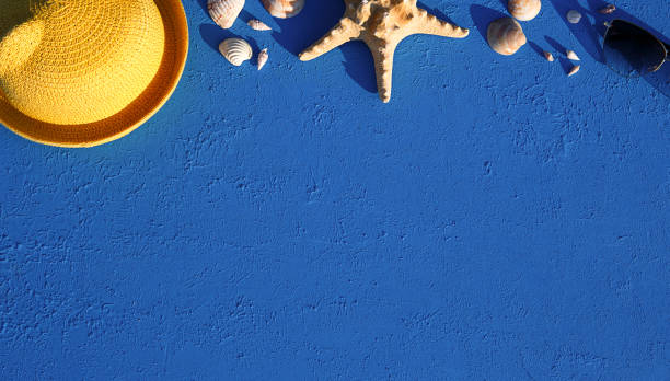 istock Frame with beach accessories on a nautical theme: yellow straw hat, sunglasses, starfish and shells on a blue background. Vacation concept, sea trip, UV protection, swimming. Copy space. Flatlay 1304714330