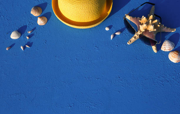 istock Frame with beach accessories on a nautical theme: yellow straw hat, sunglasses, starfish and shells on a blue background. Vacation concept, sea trip, UV protection, swimming. Copy space. Flatlay 1304714338