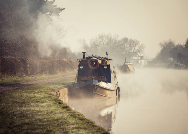 schöne neblige nebelige kanal schmale boot sonnenaufgang mit rauch aus schornstein am frühen morgen mit nebel und nebel aus dem wasser steigen, wie sonne entlang fluss in der landschaft erscheint - narrow boat stock-fotos und bilder