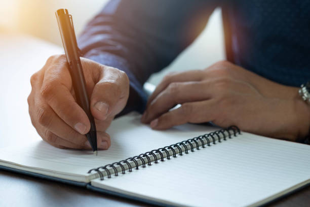 istock Close-up of man hand using writing pen memo on notebook paper or letter, diary on table desk office. Workplace for student, writer with copy space. business working and learning education concept. 1304716605