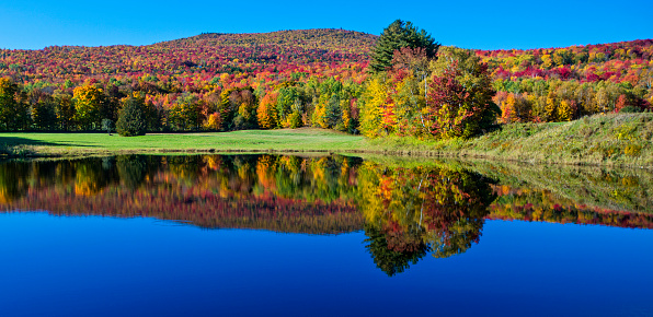 Stunning fall foliage and lake in Vermont, USA. Focus is on the middle trees on other side of the lake.