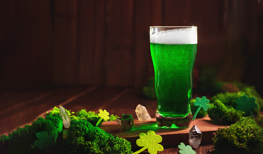 St. Patrick's Day Green Beer pint over wooden background, with shamrock leaves, harp. Patrick Day pub party, celebrating. Glass of Green beer close-up