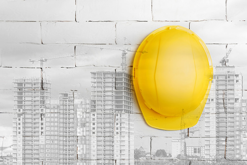 Workplace safety concept. Yellow construction helmet on a background of a white brick wall and buildings under construction. Multi-exposure.