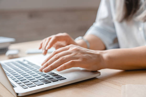Cropped shot of woman`s hands typing on laptop in office stock photo