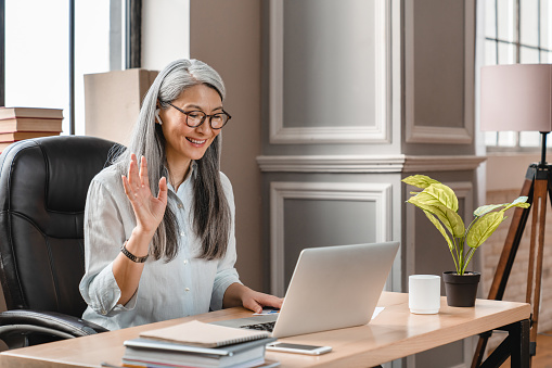 Cheerful middle-aged woman having video call on laptop at the office desk