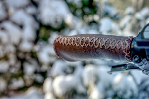 Handlebar grip covered with leather in front of a blurry background with snow covered bushes, detail shot