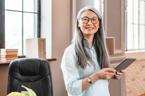 Smiling confident caucasian mature woman using tablet in office