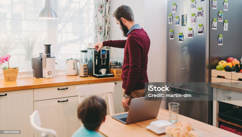 Man working at home making coffee using an espresso machine, COVID-19 home office Man taking care of son and working home during COVID-19 pandemic Coffee Maker Stock Photo