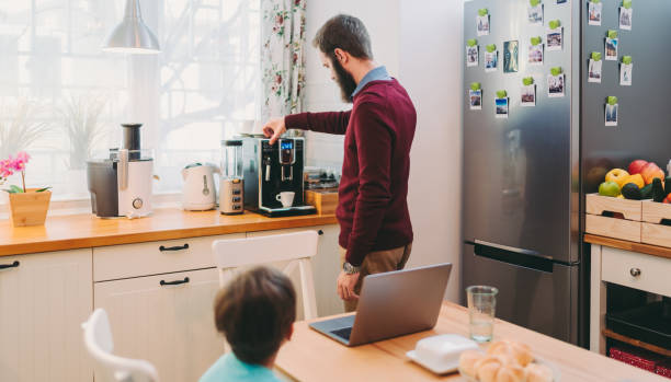Man working at home making coffee using an espresso machine, COVID-19 home office Man taking care of son and working home during COVID-19 pandemic espresso maker stock pictures, royalty-free photos & images