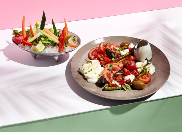 istock Tomato, olives and mozzarella salad . Restaurant appetizer plate on white table with pink wall. Day sunlight with hard shadow of fern palm leaves. Summer or spring restaurant food concept 1304729810