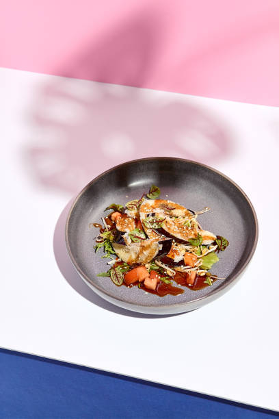 istock Eggplant restaurant appetizer plate. Restaurant appetizer food plate on white table with pink wall. Day sunlight with hard shadow of monstera palm leaves. Summer or spring restaurant food concept. 1304729978