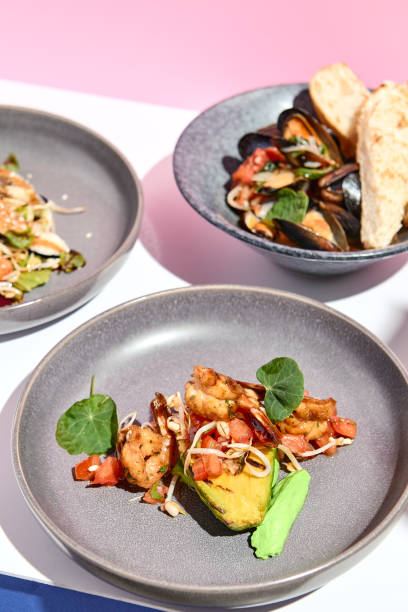 istock Shrimp and Avocado Grill restaurant plate. Restaurant appetizer food plate on white table with pink wall. Day sunlight with hard shadow of monstera palm leaves. Summer or spring restaurant food concept. 1304729994