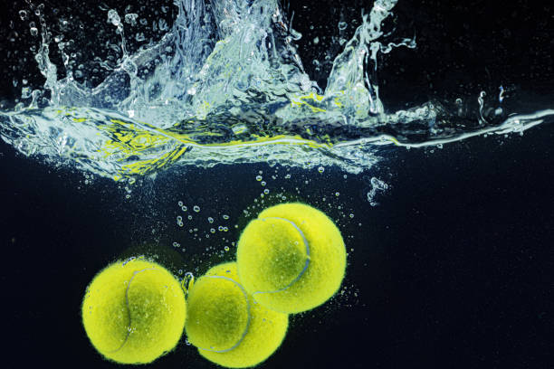 istock Tennis ball falling in water with a splash against dark background 1304730670