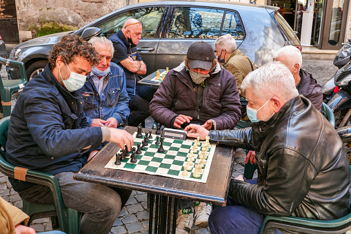 Rome, Italy, February 26 - A group of senior friends play chess at the time of Covid-19 in Piazza del Fico, near Piazza Navona, in a popular area of the historic center of the eternal city much loved by tourists and Romans for the presence of restaurants, cafes, pubs and places of art and culture. Image in High Definition format.