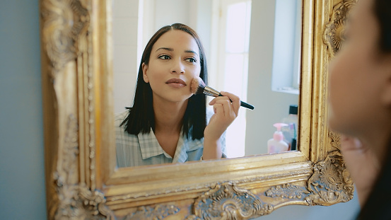 Cropped shot of an attractive young woman using a mirror to put her makeup on at home