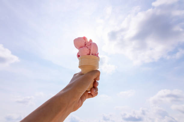 istock Hand holding ice cream cone against the sun on sky background, summer day. 1304739358
