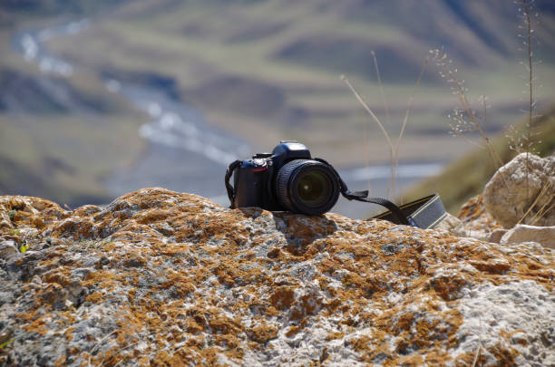 istock Modern camera on rock in the sunny day with mountain valley view background. 1304741915