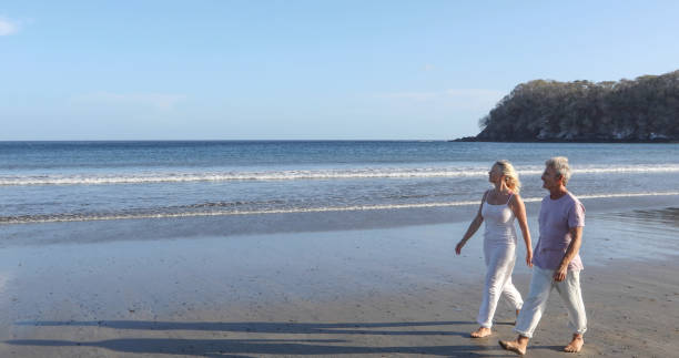 istock Mature couple walk down sandy beach in the morning 1304742627