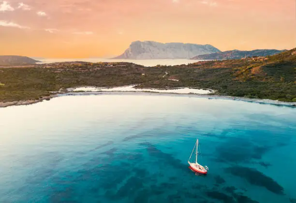 View from above, stunning aerial view of a sail boat sailing on a turquoise and transparent water. Sardinia, Italy.