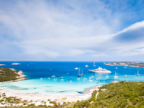 View from above, stunning aerial view of the Grande Pevero beach with boats and luxury yachts sailing on a turquoise, clear water. Sardinia, Italy.