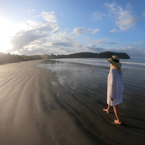 istock Woman walks down sandy beach at sunrise 1304742826