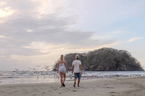 istock Mature couple walk down sandy beach in the morning 1304742847