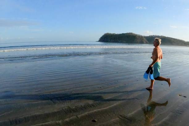 l'uomo corre giù per la spiaggia con attrezzature snorkling all'alba - men beach running shirtless foto e immagini stock