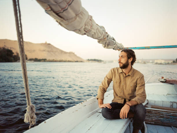 Man traveling on felucca on the Nile at sunset Young Caucasian man traveling on felucca on the Nile at sunset felucca boat stock pictures, royalty-free photos & images