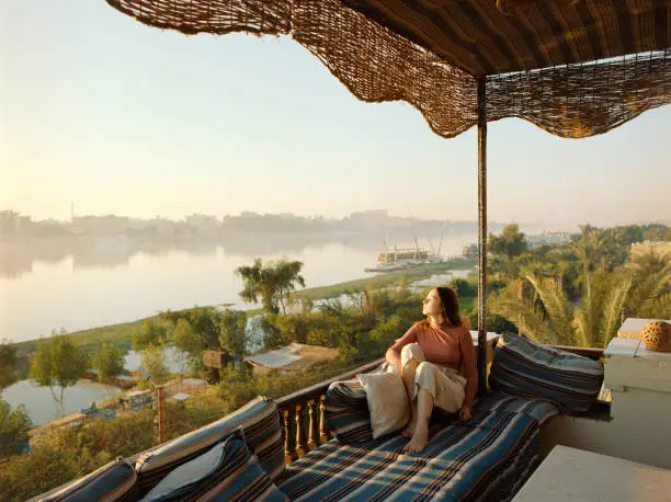 Photo of Woman sitting on terrace and looking at Nile at sunset in Luxor