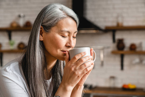 schön aussehende kaukasische reife frau trinken heißen kaffee in der küche - chinese tea stock-fotos und bilder