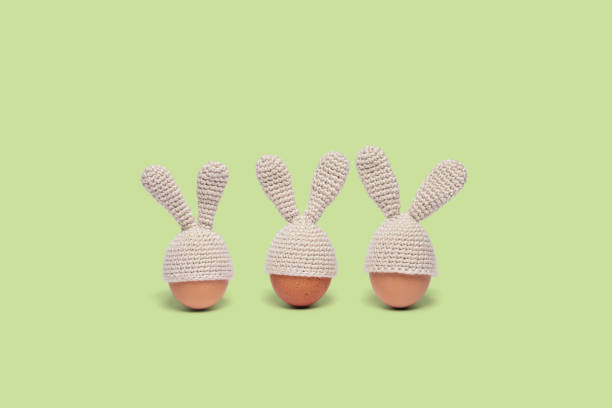Three Easter eggs in crochet hats with bunny ears isolated on green background