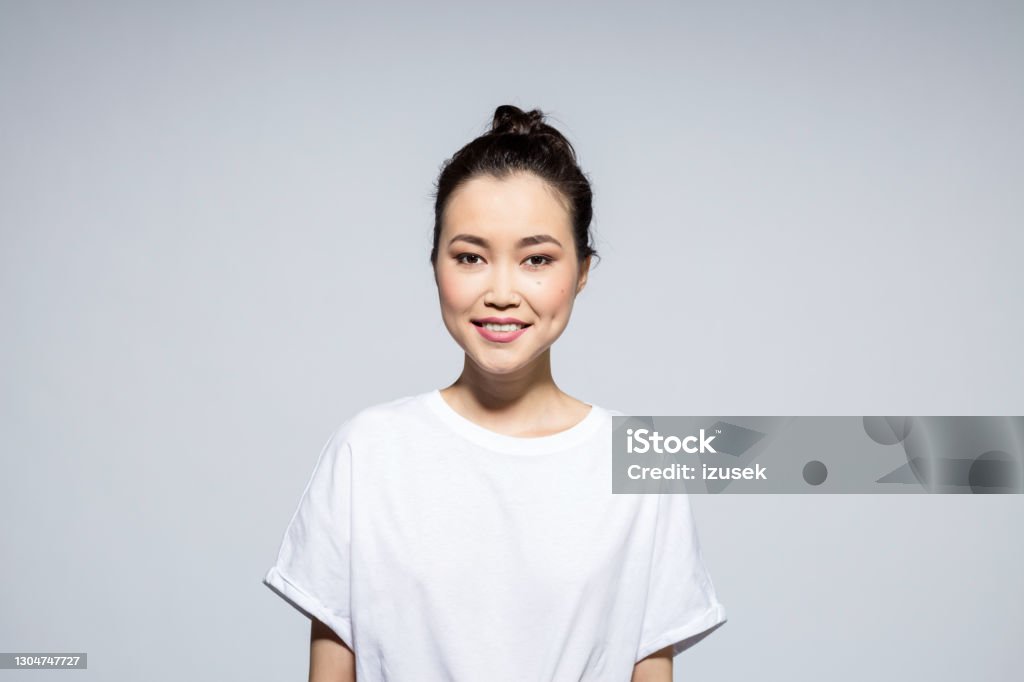 Portrait of happy asian young woman Portrait of beautiful asian young woman wearing white t-shirt, smiling at camera. Studio shot, grey background. T-Shirt Stock Photo
