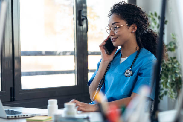 istock Attractive young afro female doctor talking with smart phone while working with her computer in the consultation. 1304748732