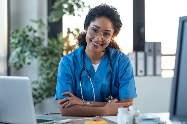 istock Attractive afro female doctor smiling looking at camera while working with laptop in the consultation. 1304748782