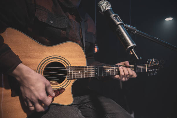 da vicino un uomo suona una chitarra acustica in una stanza buia. - microphone stage music popular music concert foto e immagini stock