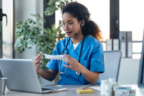 istock Attractive afro female doctor talking while explaining to her patient how to put on surgical mark through a video call with laptop in the consultation. 1304748967