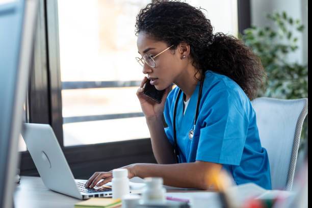 istock Attractive young afro female doctor talking with smart phone while working with her computer in the consultation. 1304749177