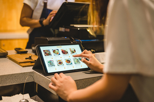 Close-up of hand young Asian woman use digital tablet to buying food on digital tablet at cashier counter.