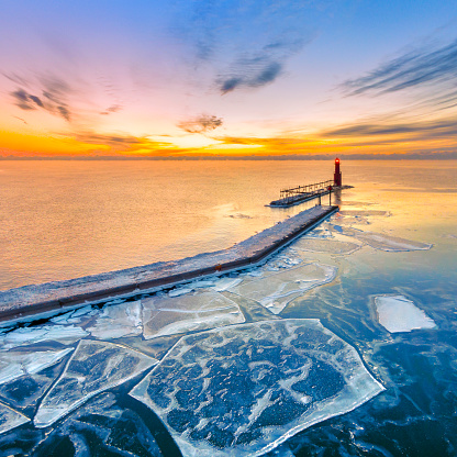 Scenic Winter aerial view of lighthouse before the colorful dawn sky. The calm water inside of the harbor freezes before the more active waters of Lake Michigan.