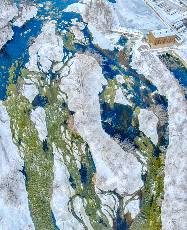 Looking straight down on river rapids in winter, many icy islands, trees coated in ice and snow. This is the Fox River in Kaukauna, Wisconsin.