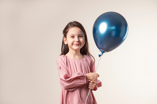 Girl is looking at camera and holding blue balloon.