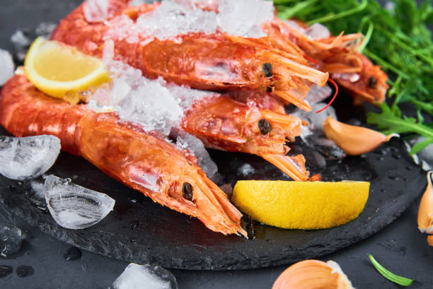 istock Frozen seafood. Fresh shrimps with lemon on dark background. Red raw prawns 1304758904