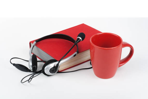 istock Audiobook on white background. Headphones put over book, empty cover, red cup, copy space for ad text. Distance education, e-learning concept. 1304763575