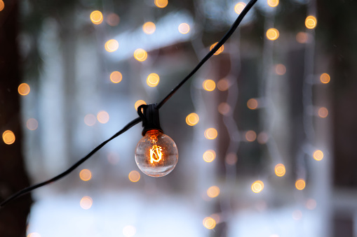 Close-up view of illuminated retro light bulb hanging outdoors and lighting garlands as Christmas decoration in cold day of December