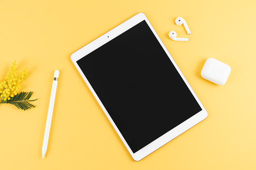 Tablet with headphones and pencil on yellow background. Top view. Copy space.